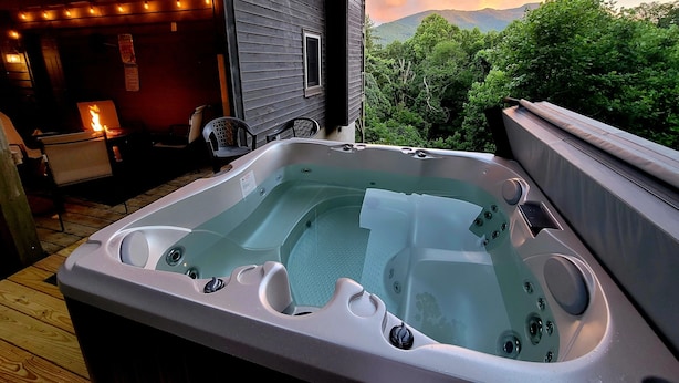 Un bain à remous sur une terrasse en bois, avec vue sur les montagnes et les arbres.