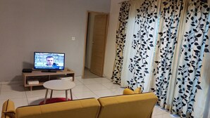 Olohuoneessa on televisio puisen jalustan päällä, pieni pyöreä pöytä ja keltainen sohva.