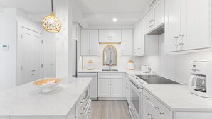 Une cuisine moderne avec des meubles blancs, un plan de travail en marbre, un îlot central et un luminaire suspendu original.