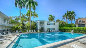 Une piscine avec des chaises longues, des palmiers et un bâtiment doté de balcons.