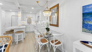 Une cuisine moderne avec des meubles blancs, une table à manger en verre et des chaises blanches.