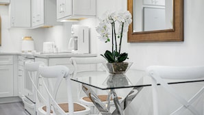 Une cuisine moderne avec des meubles blancs, une table à manger en verre et des chaises blanches.