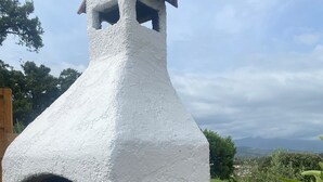 Un four en briques blanches avec une cheminée, une lanterne et un vase décoratif sur une terrasse carrelée.