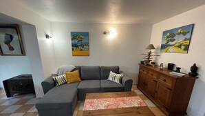 Un salon avec un canapé d’angle gris, une table basse en bois, un meuble contenant des objets décoratifs et deux tableaux accrochés aux murs.