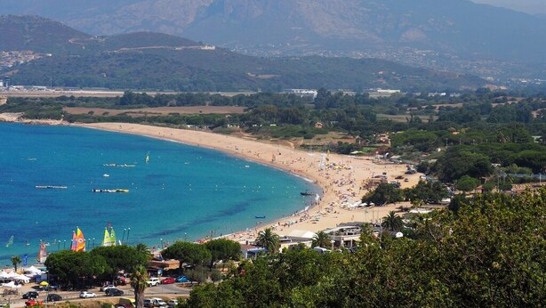 Une ville côtière dotée d’une plage, d’une mer d’un bleu limpide et de montagnes en arrière-plan.