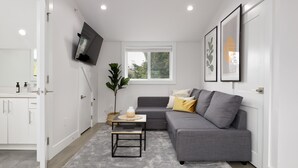Una sala de estar moderna con un sofá gris, una mesita, una planta en maceta y un ventanal.