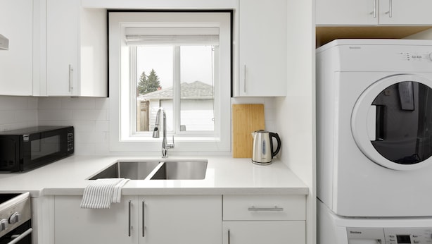 Una cocina moderna con armarios blancos, un lavamanos de acero inoxidable, un microondas, un hervidor y una lavadora de carga frontal.