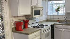 A kitchen with white cabinets, a microwave, a gas stove, and a sink. - Convenient One Bedroom Hancock Condo (Austin)