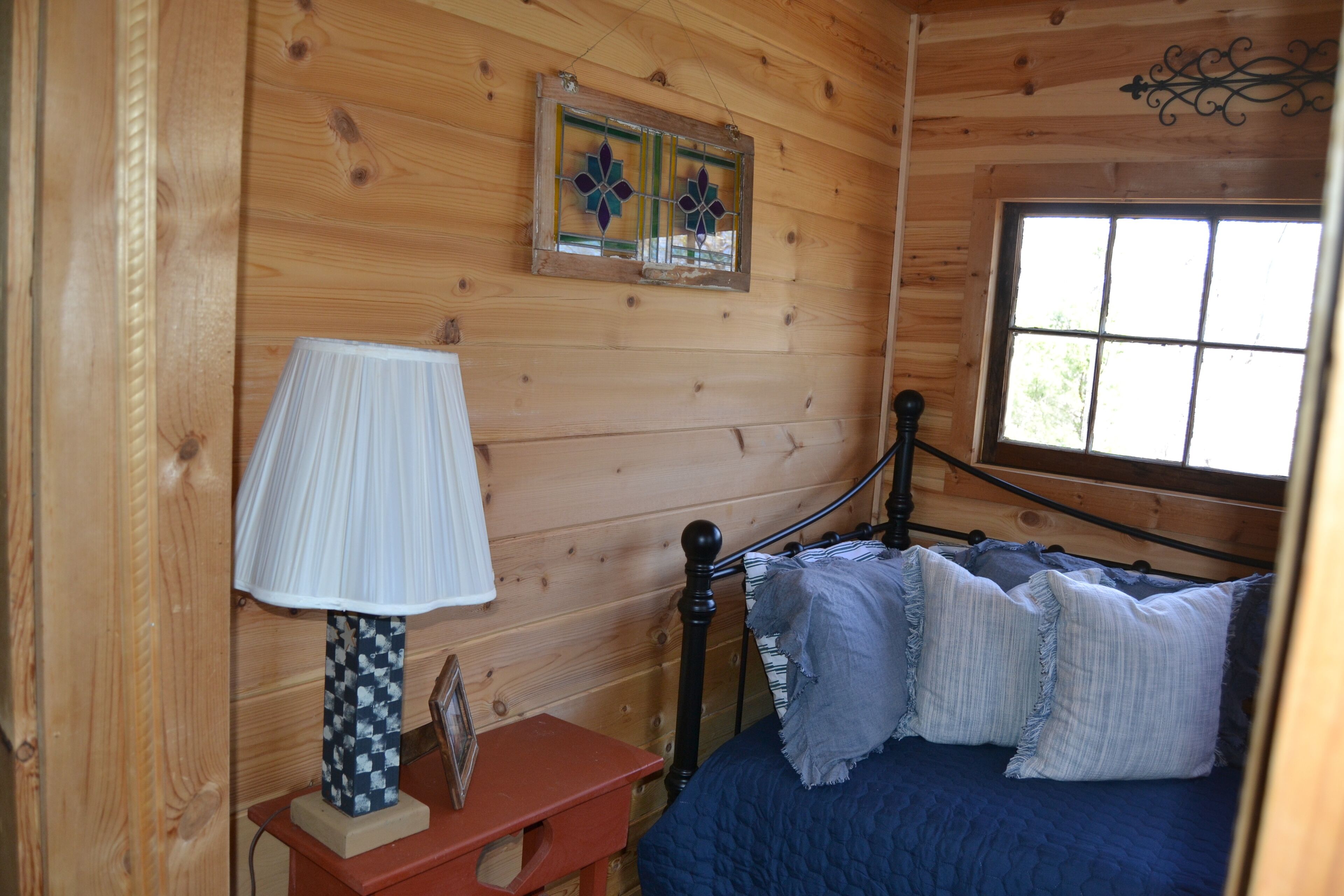 A wooden cabin room with a bed, a nightstand, a lamp, and a window.
