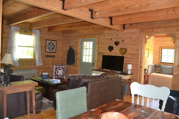 L’intérieur chaleureux d’un chalet, avec un revêtement mural en bois, un canapé, une table à manger et un téléviseur.