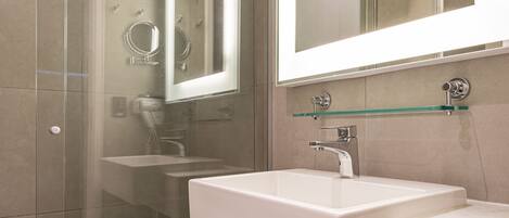 Un baño moderno con ducha envuelta en vidrio, un espejo grande y un mueble de tocador con doble lavamanos.