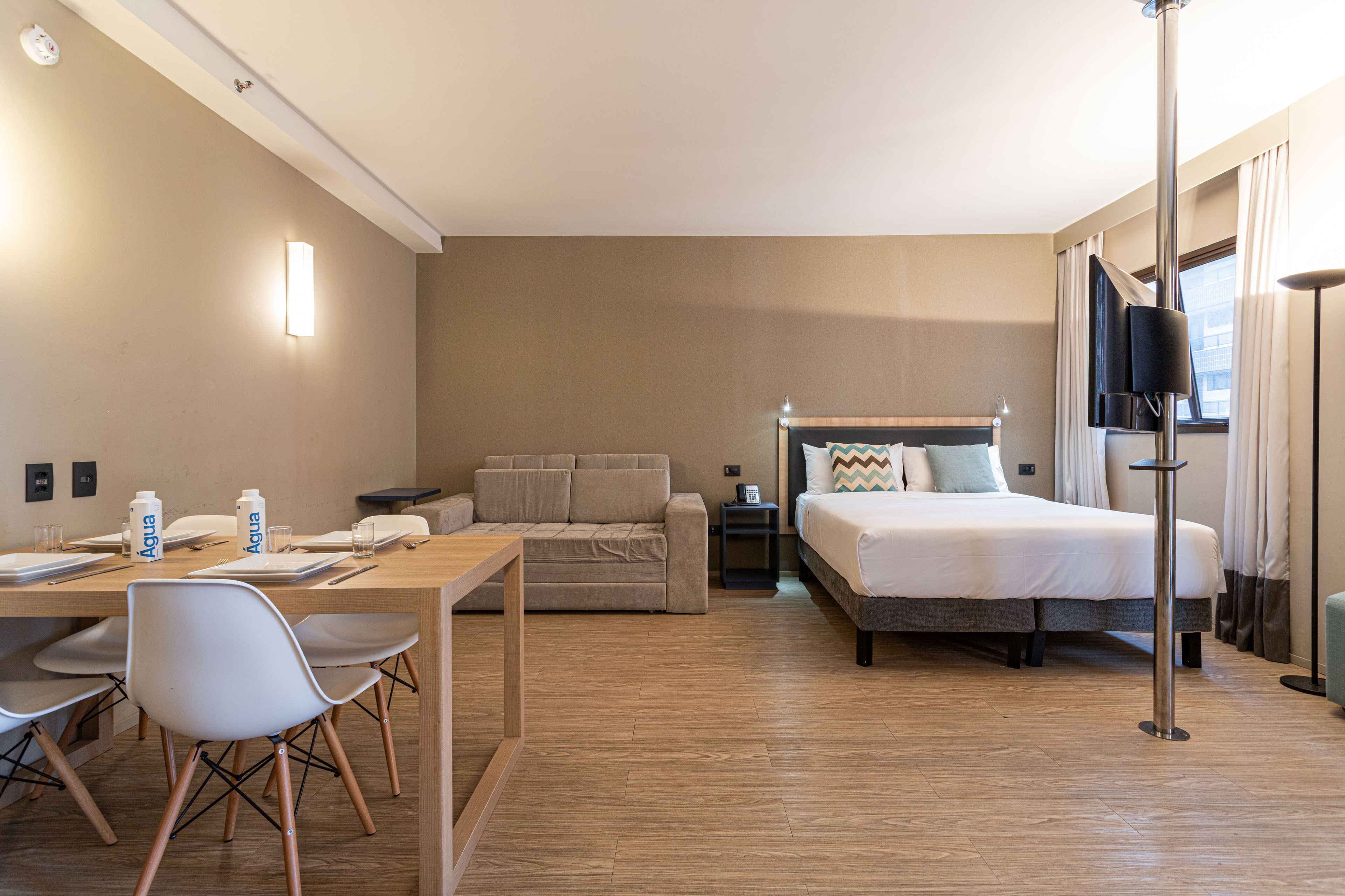 Et hotelværelse med seng, sofa, skrivebord med stole, et sengebord og et fjernsyn.