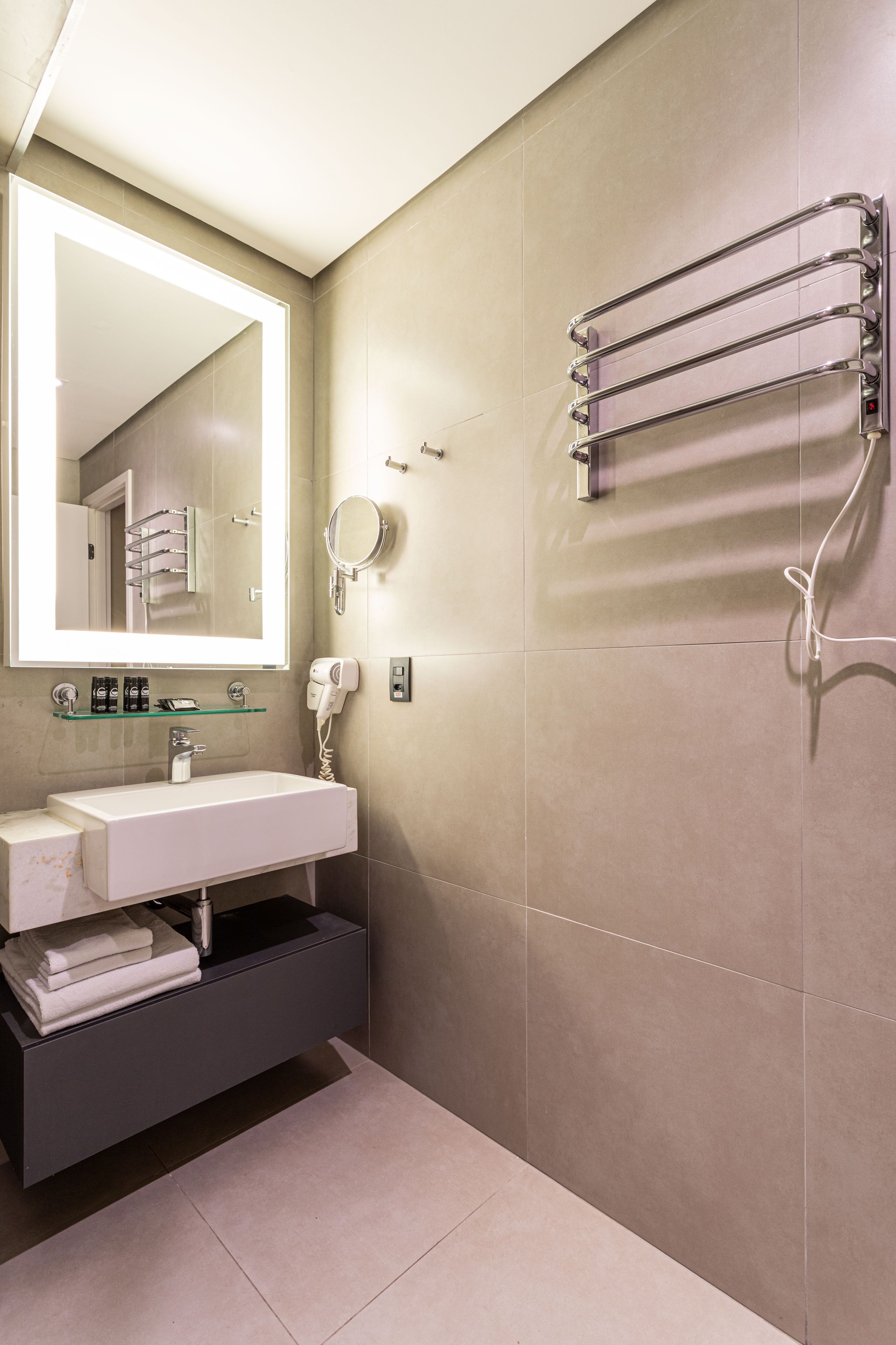 Un bagno moderno con uno specchio grande, un lavandino, un porta asciugamani e un soffione doccia manuale.