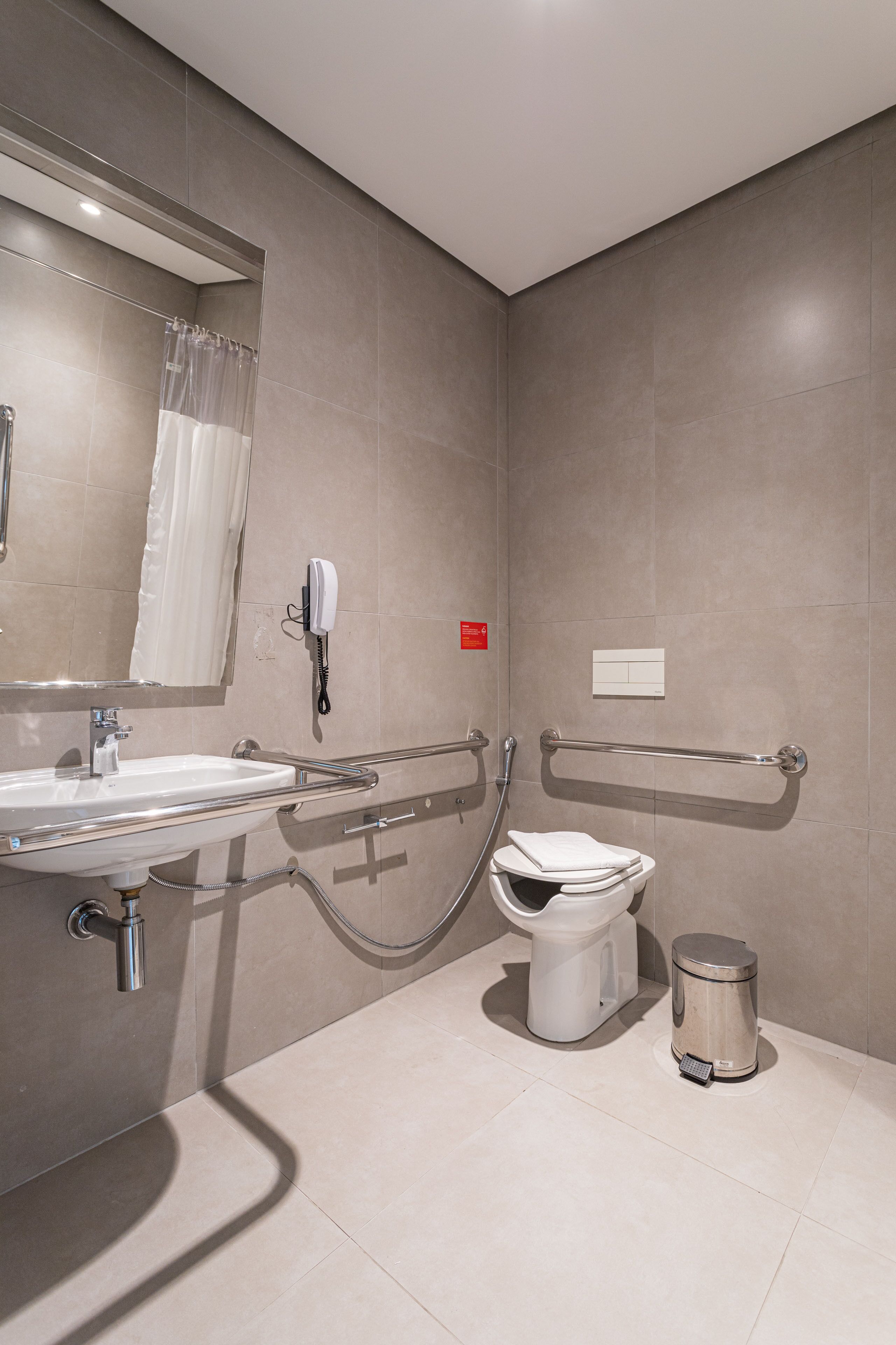 A modern bathroom with a sink, mirror, toilet, and handrail.