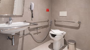 A modern bathroom with a sink, mirror, toilet, and handrail.