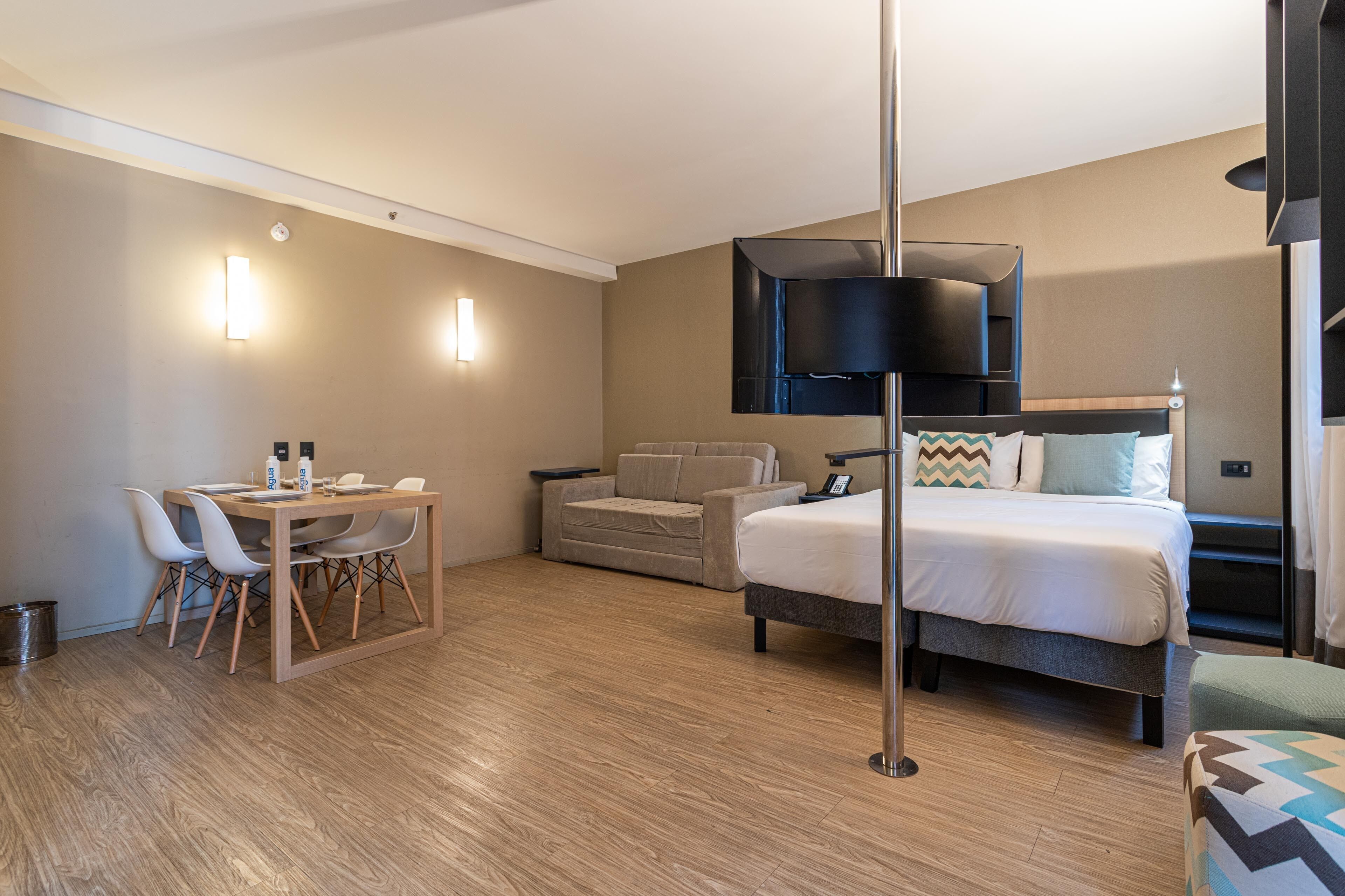 Une chambre d’hôtel comprenant un lit, un bureau avec des chaises, un canapé et un téléviseur à écran plat fixé au mur.