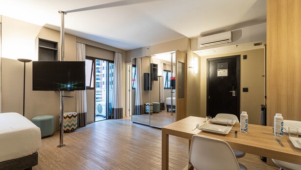 A hotel room with a bed, a desk with a chair, a television, and a mirror. - Charlie Alphaville  (Barueri)