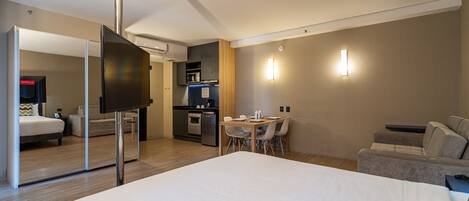 A hotel room with a bed, a TV, a dining table with chairs, a kitchenette, and a sofa.