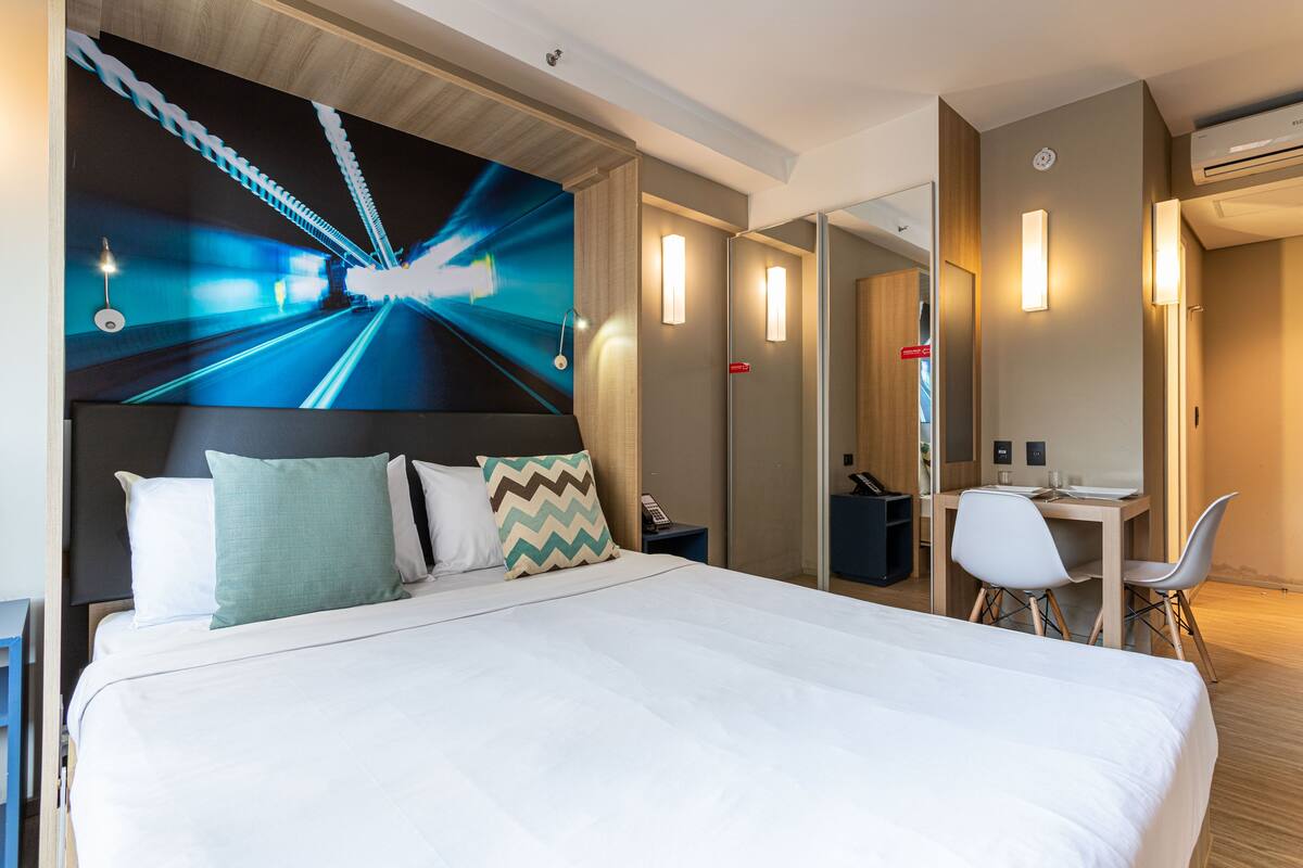 Quarto de hotel moderno com uma cama grande, uma escrivaninha e um espelho.