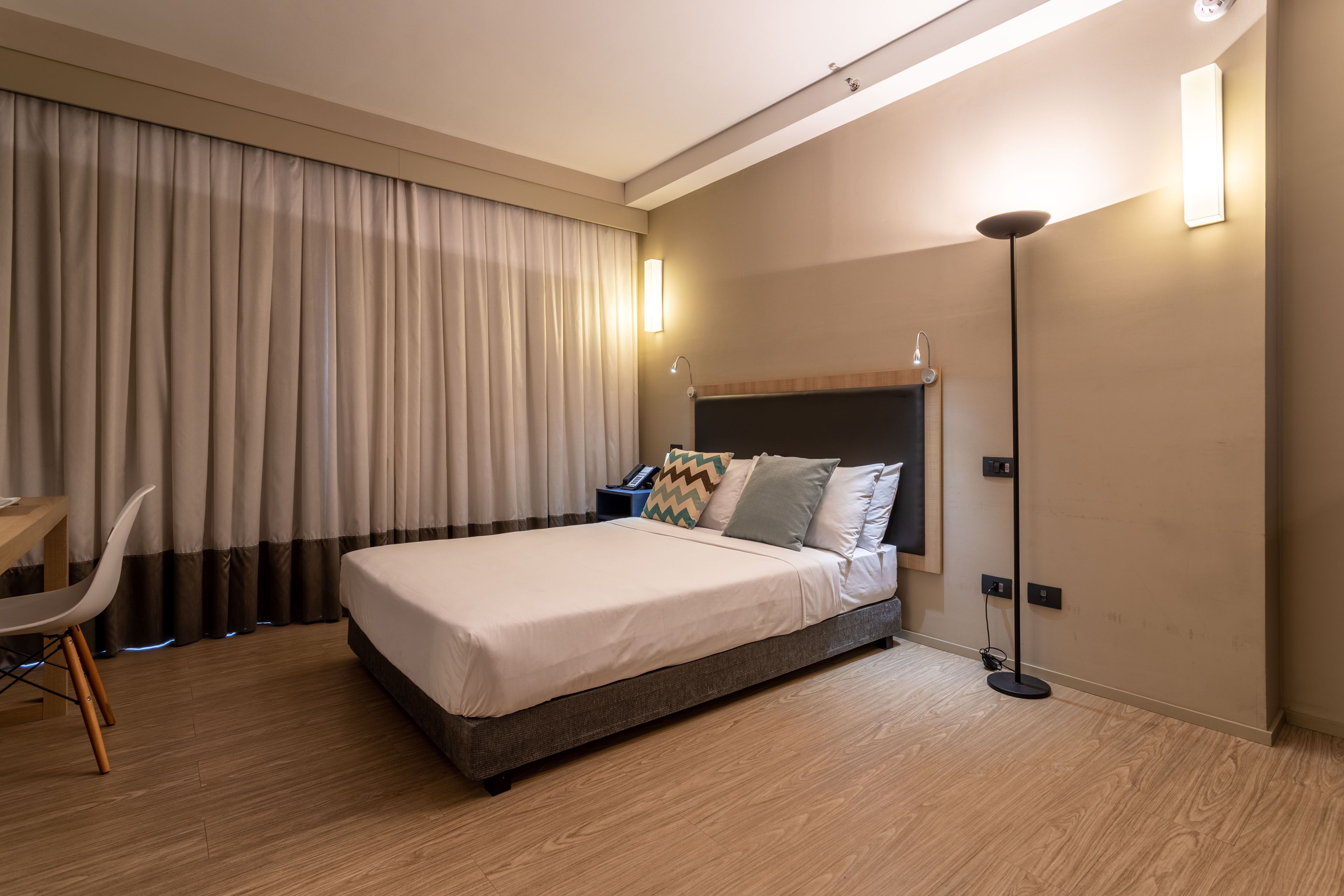 A modern hotel room with a large bed, a desk, and a chair.