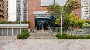 A modern building entrance with a glass facade, a palm tree, and a staircase leading to the entrance. - Charlie Alphaville  (Barueri)