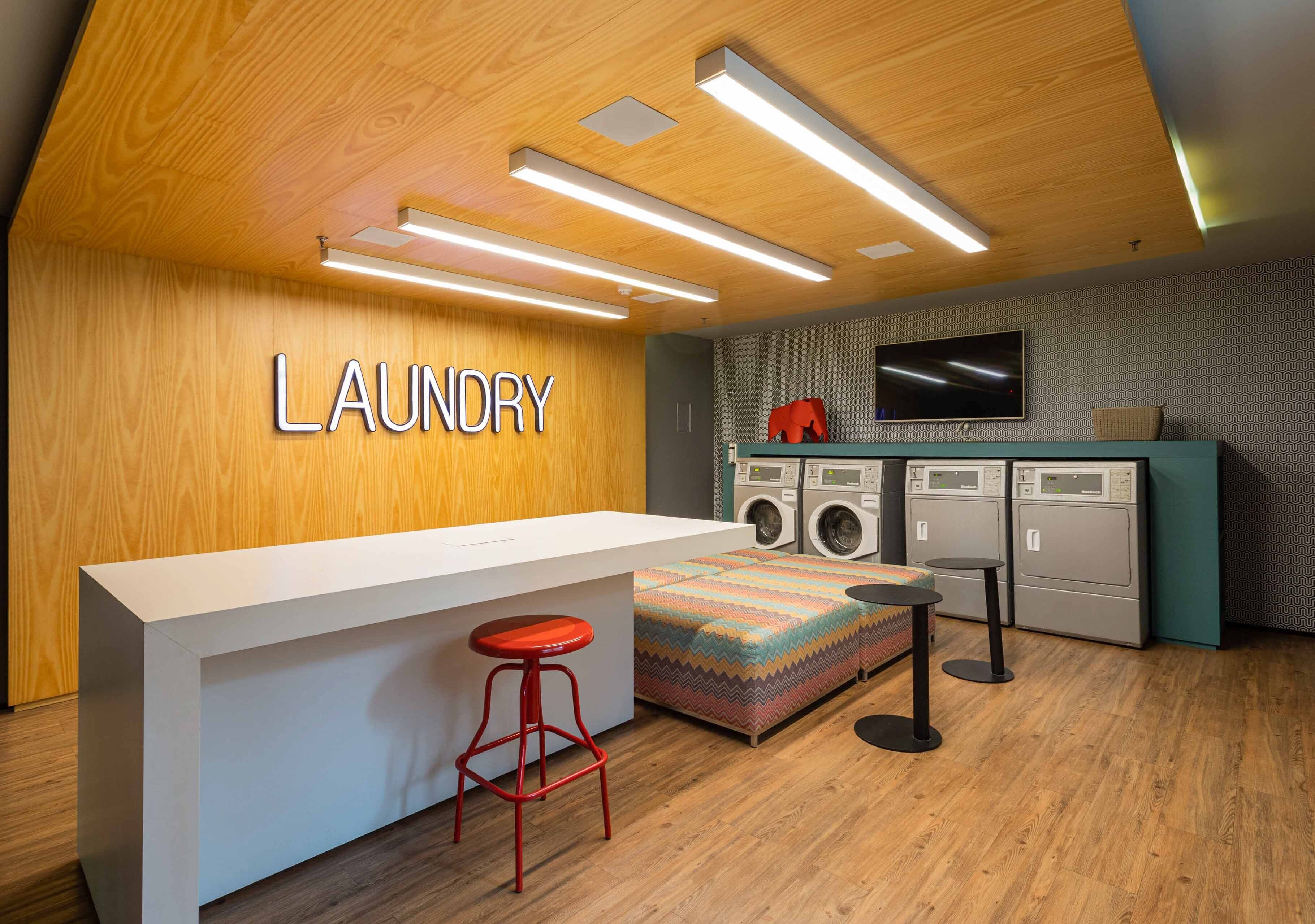 A laundry area with a wooden wall, a washing machine, a dryer, a television, and a bar stool.