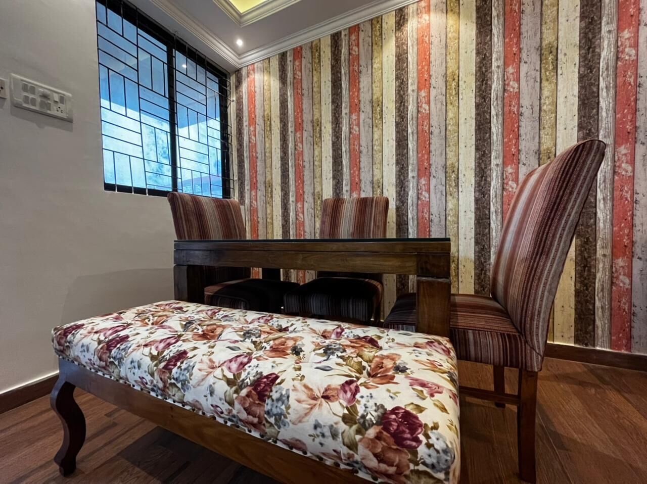 Een kamer met een bed, een stoel, een houten bankje en behang met strepen.