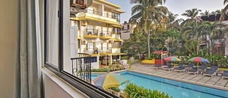 A hotel with a pool, outdoor seating, and palm trees.