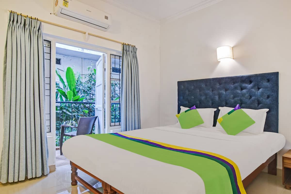 Un dormitorio con una cama grande, cabecera, mesita de noche y ventana con cortinas.