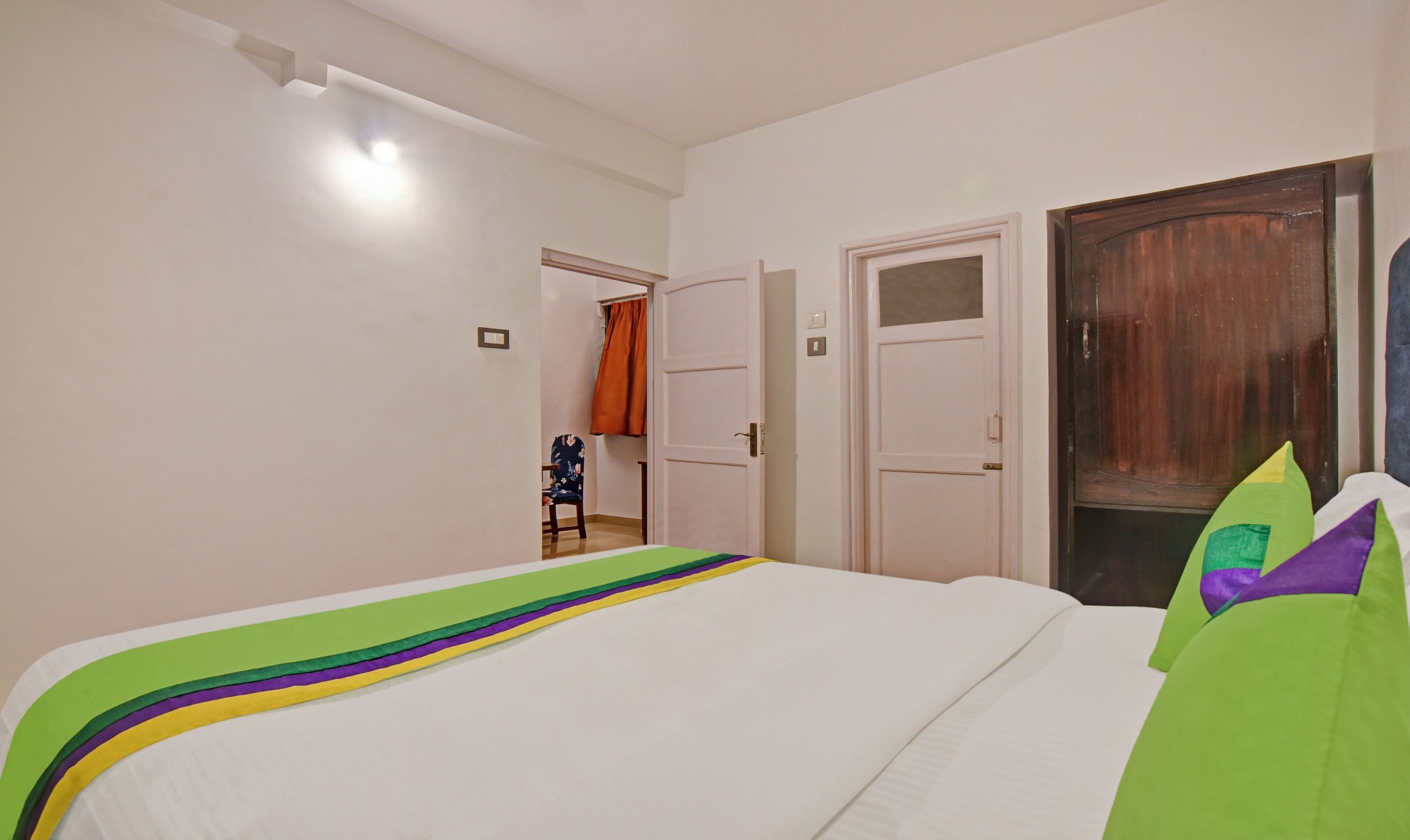 A bedroom with a bed, a door, and a view into another room.