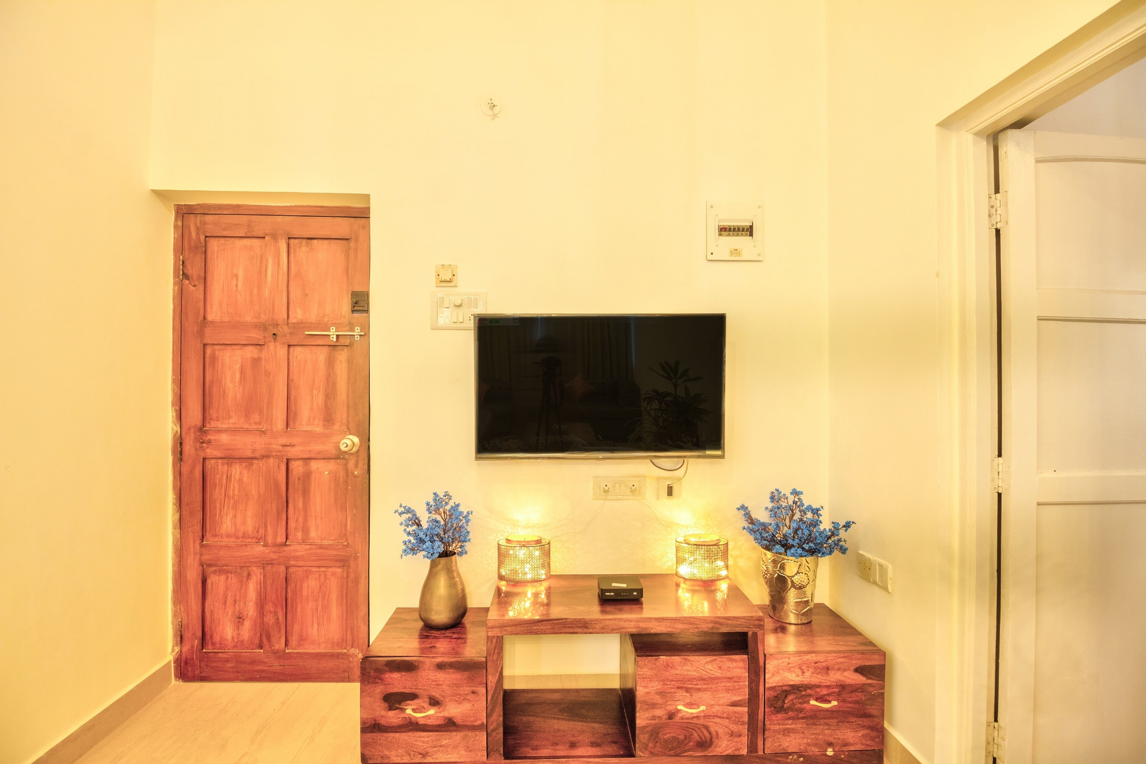 A hallway with a wooden door, a television mounted on the wall, and two decorative vases with blue flowers.