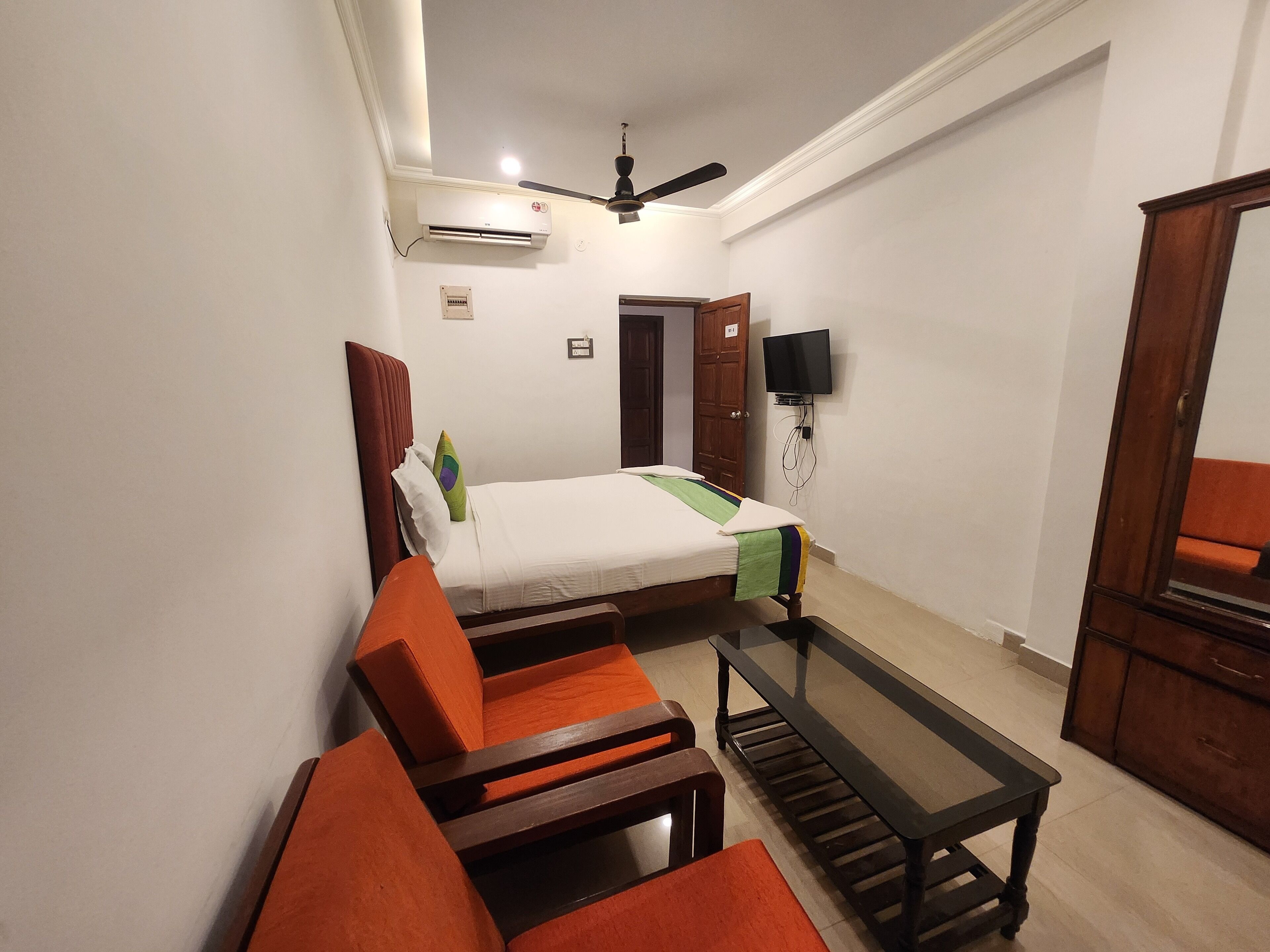 A hotel room with a bed, a TV mounted on the wall, a ceiling fan, and a small table.
