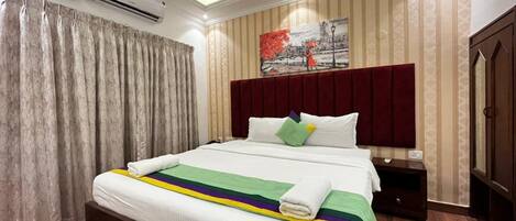 Une chambre d’hôtel avec un grand lit, une table de chevet, un appareil de climatisation et un ventilateur de plafond.