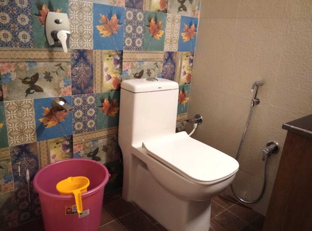A bathroom with a toilet, a shower, and a bucket with a yellow scoop.