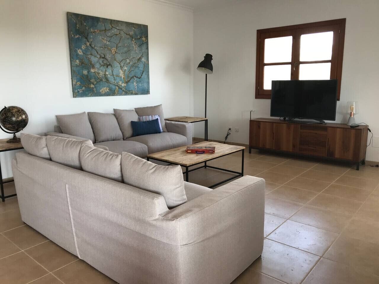 Un saló amb un sofà beix, una taula de centre, una televisió i un armari de fusta.