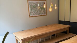 Een houten eettafel met banken, een hangende lamp en een lijstwerk met kunst aan de muur.