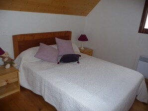 Une chambre à coucher avec un plafond en bois, un lit avec une literie blanche, deux tables de chevet et une petite table de nuit avec une lampe.