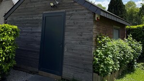 Een klein houten gebouw met een donkere deur, een lamp en een klein raam.