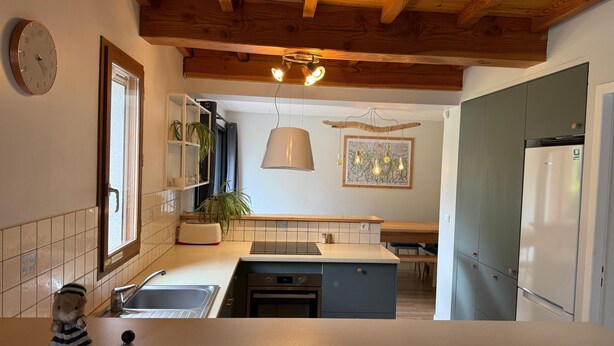 Een keuken met houten balken, een klok, een spoelbak, een fornuis en een koelkast.