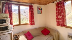 Ein gemütliches Zimmer mit Holzbalkendecke, einem beigen Sofa mit roten Kissen, einer Mikrowelle und einer Waschmaschine.