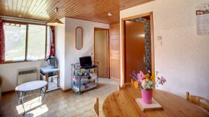 Ein Zimmer mit Holzboden, einem Esstisch mit Stühlen, einem kleinen runden Tisch mit einem Sessel, einem Bücherregal und einer Tür zu einem anderen Raum.