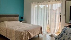 Un dormitorio con cama, mesita de noche, lámpara y vistas al exterior a través de cortinas translúcidas.