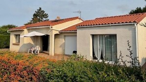 Una hilera de casas de una planta con tejados de tejas rojas, paredes color crema y un pequeño patio con mobiliario exterior.