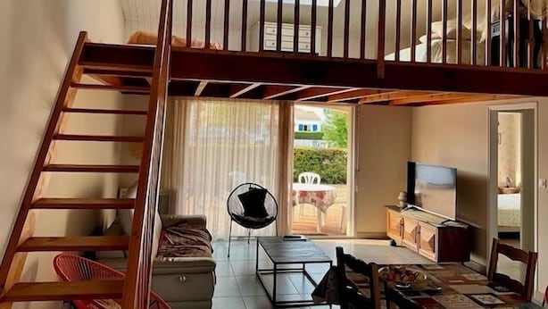 Un dormitorio estilo loft con escalera de madera, un sofá, una mesa de comedor y un televisor.