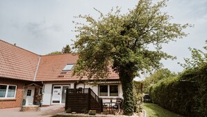 Un edifici amb teulada de rajola, zona d'estar exterior coberta i un arbre gran al davant.