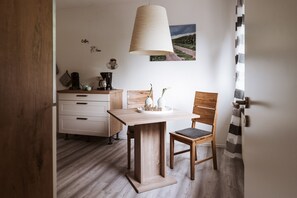 A small, modern kitchen with a wooden table and chair, a coffee maker, and a painting on the wall.