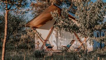 A tent-like structure with two lounge chairs, surrounded by trees and vegetation.