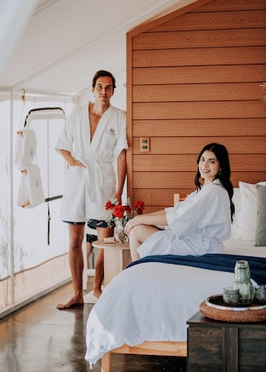 A modern bedroom with a wooden headboard, a bed with a blue blanket, and a small table with a vase of red flowers. - Salterra Glamping (Tequisquiapan)