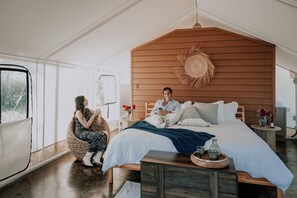 A spacious bedroom with a large bed, a wooden headboard, and a wicker chair. - Salterra Glamping (Tequisquiapan)