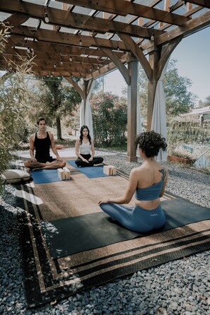 Three people sitting on yoga mats under a wooden pergola in an outdoor setting. - Salterra Glamping (Tequisquiapan)